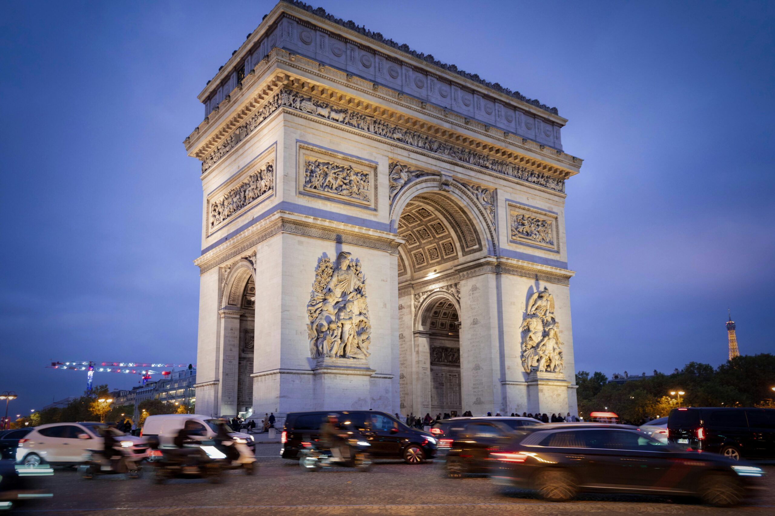 Iconic Arc de Triomphe under blue evening sky with bustling traffic in Paris.